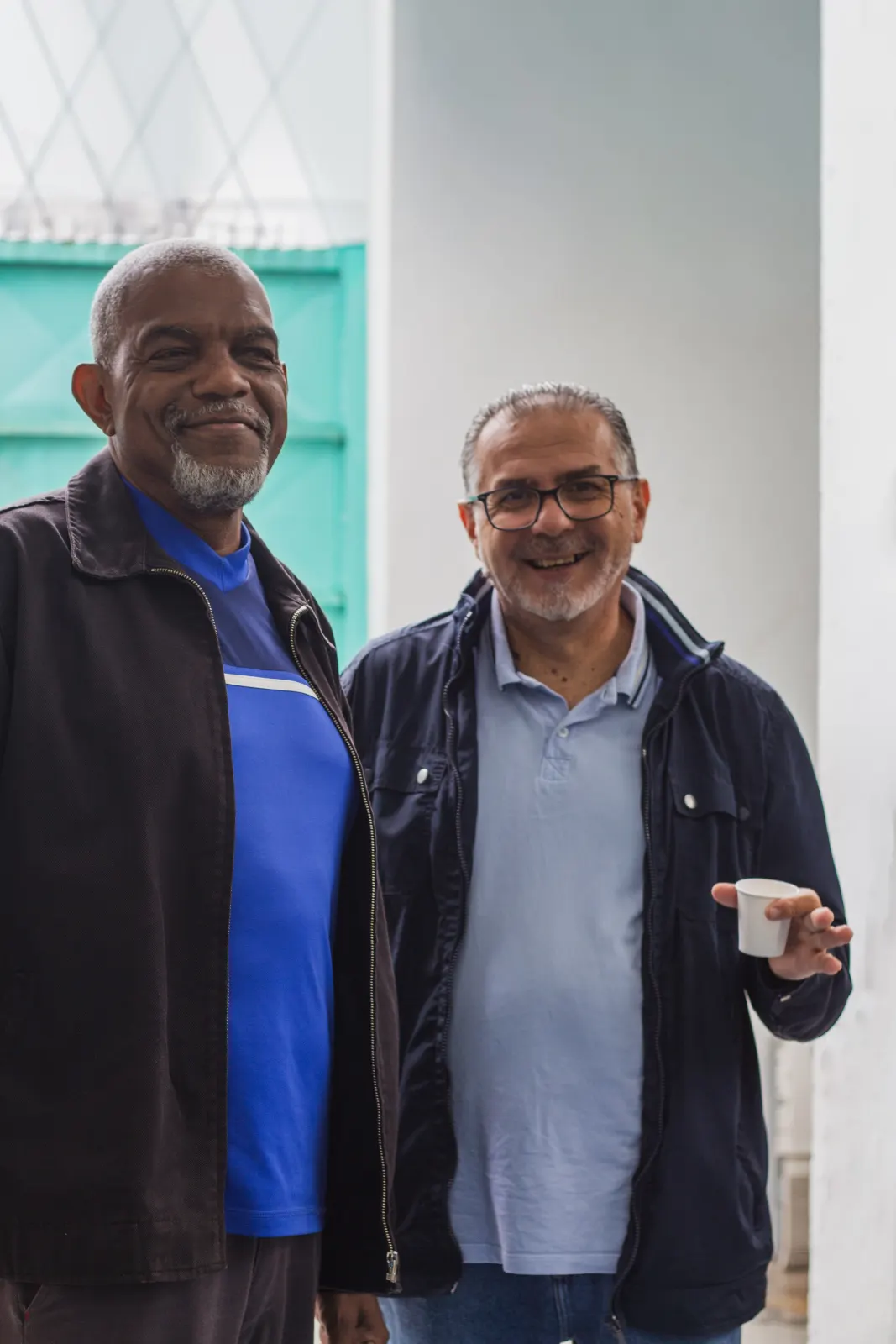 Dois irmãos da igreja, sorrindo lado a lado na entrada do templo.