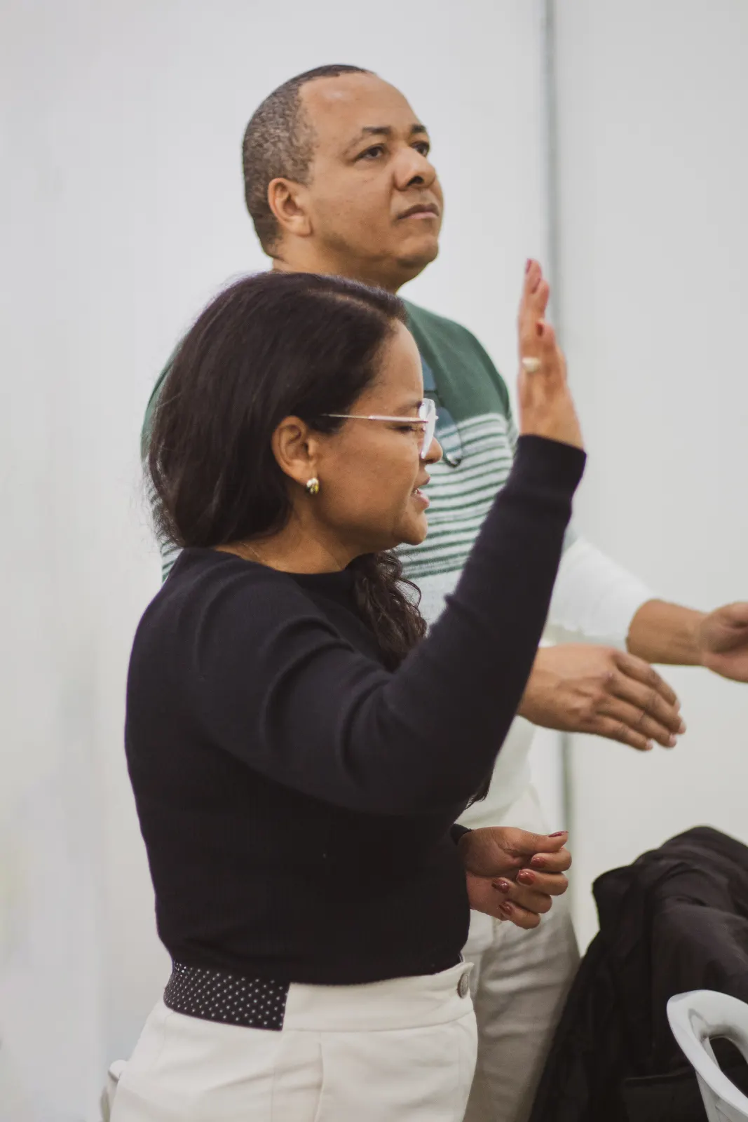 Mulher de mão erguida, cantando de olhos fechados, ao lado de outros irmãos em pé no louvor.